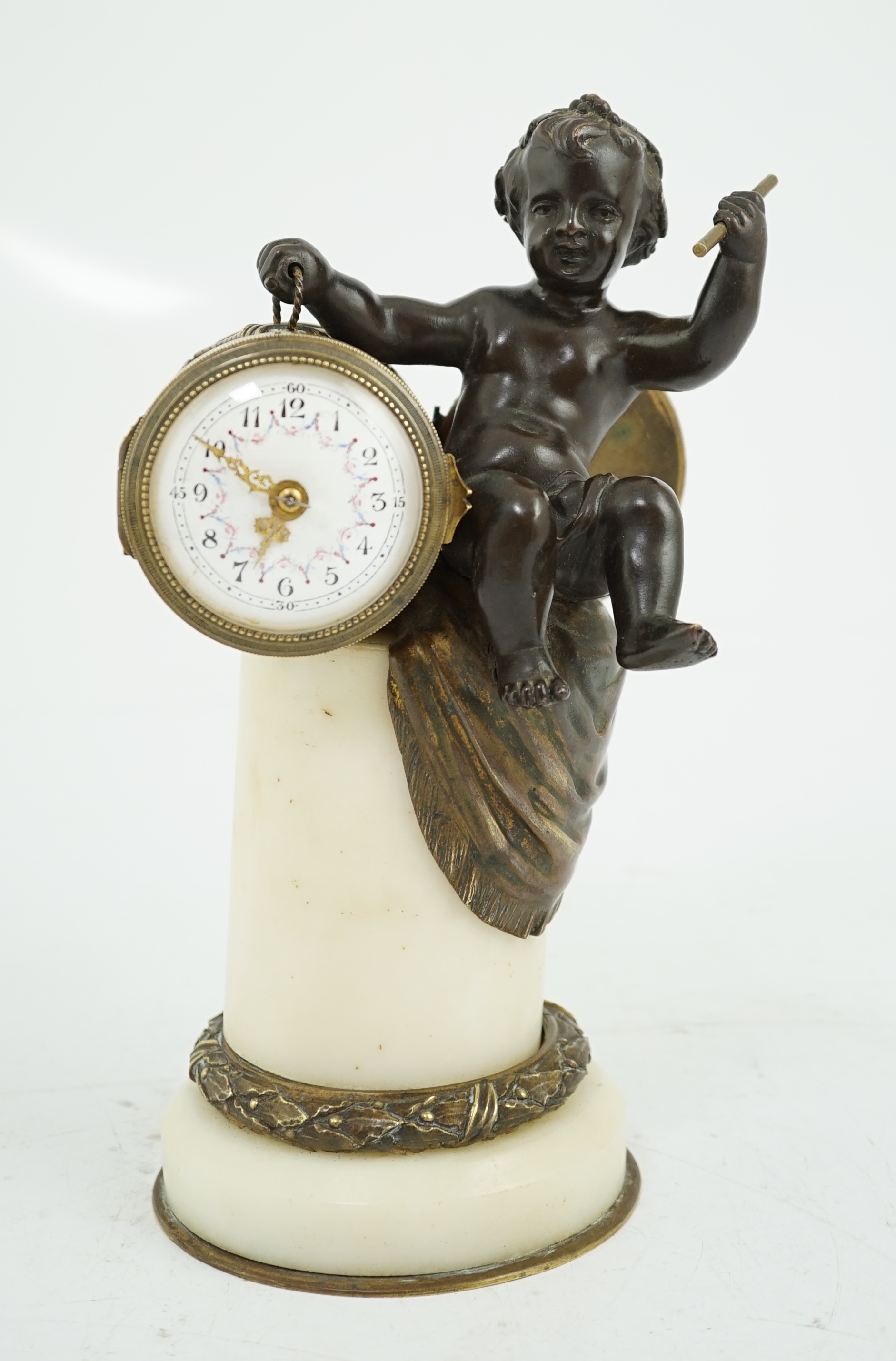 An early 20th century French eight day bronze and ormolu desk timepiece modelled as a putto banging upon a drum, with floral enamelled dial and white marble plinth, 12cm wide, 22.5cm high. Condition - good